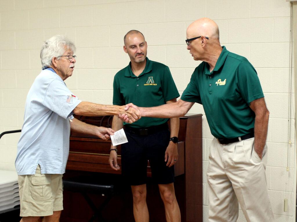 Lion Horace presents the check to Coach Gilles and Coach Roy